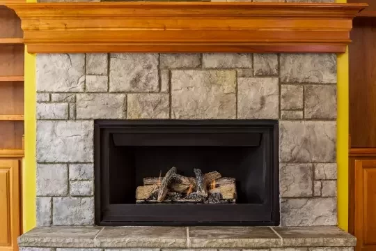 A gas fireplace in a stone and wood wall.