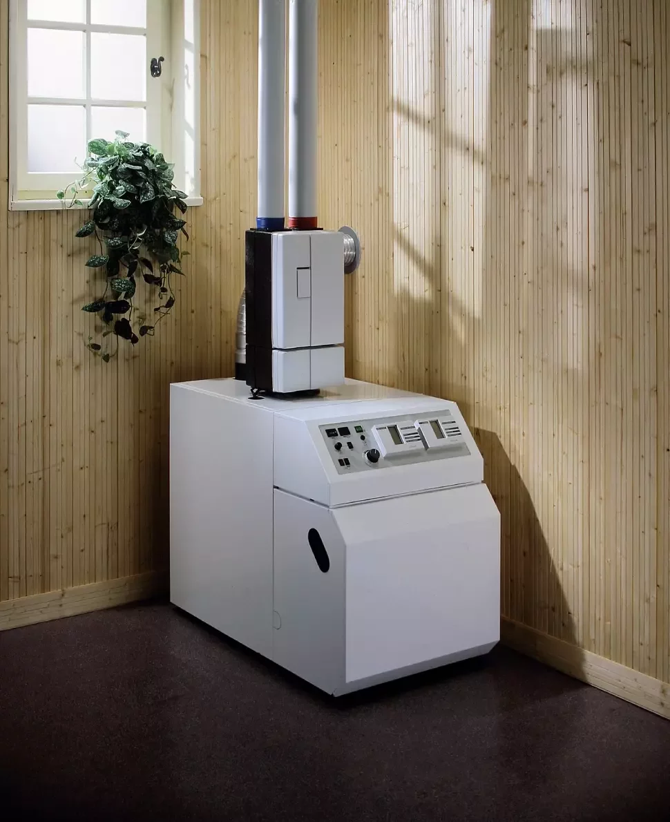A white boiler unit in a wood-walled room. A plant sits on a windowsill.