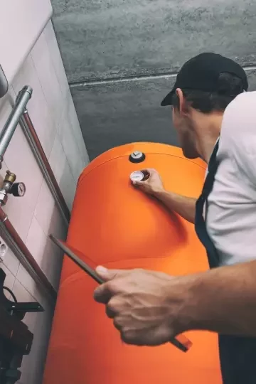 An engineer adjusts levels on an orange boiler with one hand, and holds a tablet with the other.