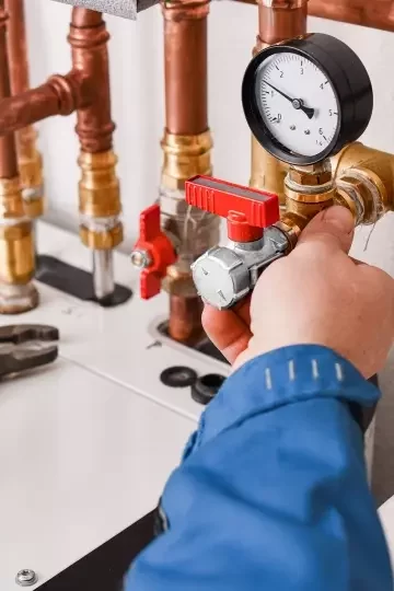 The hand of a plumber reaches to adjust some pipes.