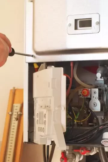 A boiler panel is opened to reveal the inside, as a hand uses a screwdriver to fix a screw into the boiler.